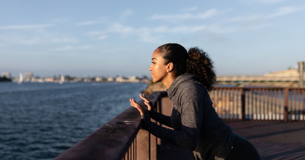 Fit woman performing exercises on a scenic waterfront pier at sunset, enjoying a healthy lifestyle outdoors.