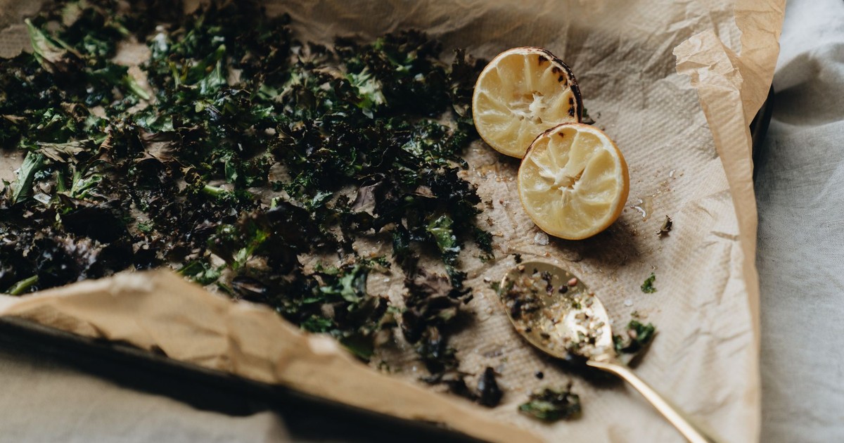 A minimalistic image of roasted herbs and lemon halves on a lined baking sheet with a spoon.