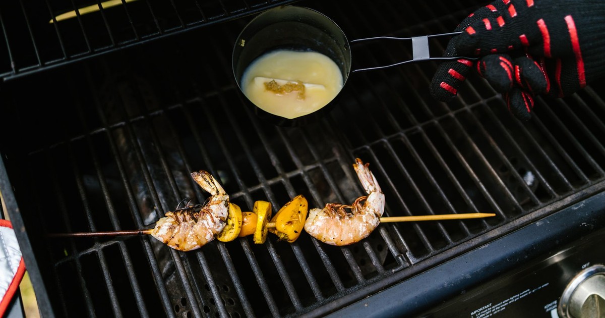 Shrimp skewers with lemon being grilled, seasoned with sauce, on an outdoor barbecue.