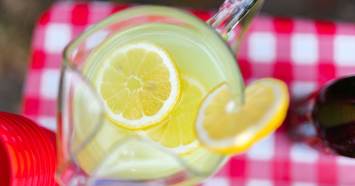 A top-view of lemonade with lemon slices in a pitcher on a checkered picnic table.