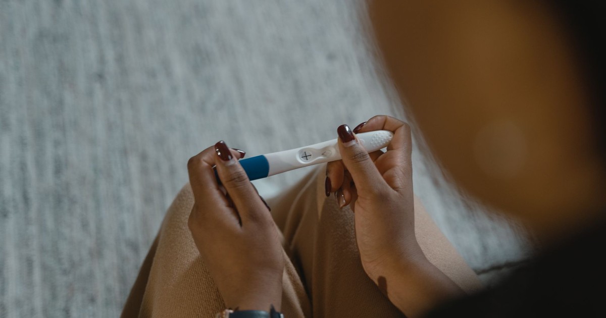 Close-up of a woman holding a positive pregnancy test with a plus sign, symbolizing new beginnings.