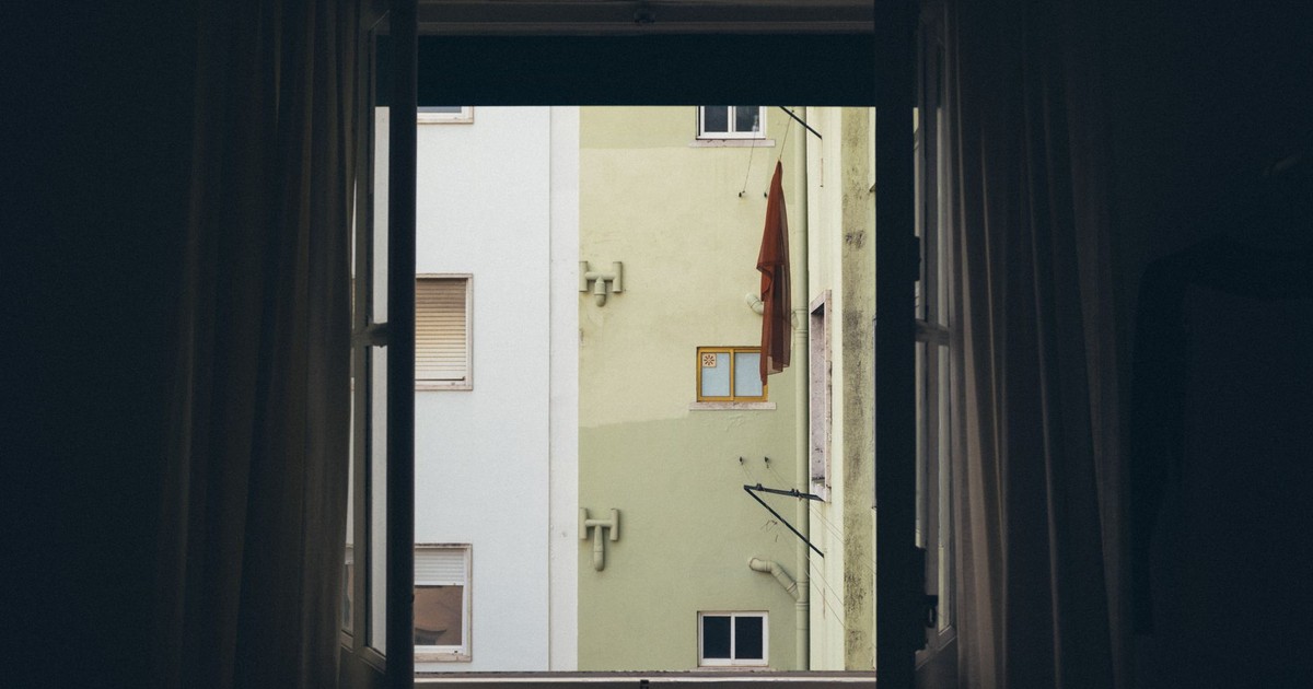 A view of an urban apartment building facade framed by an open window.