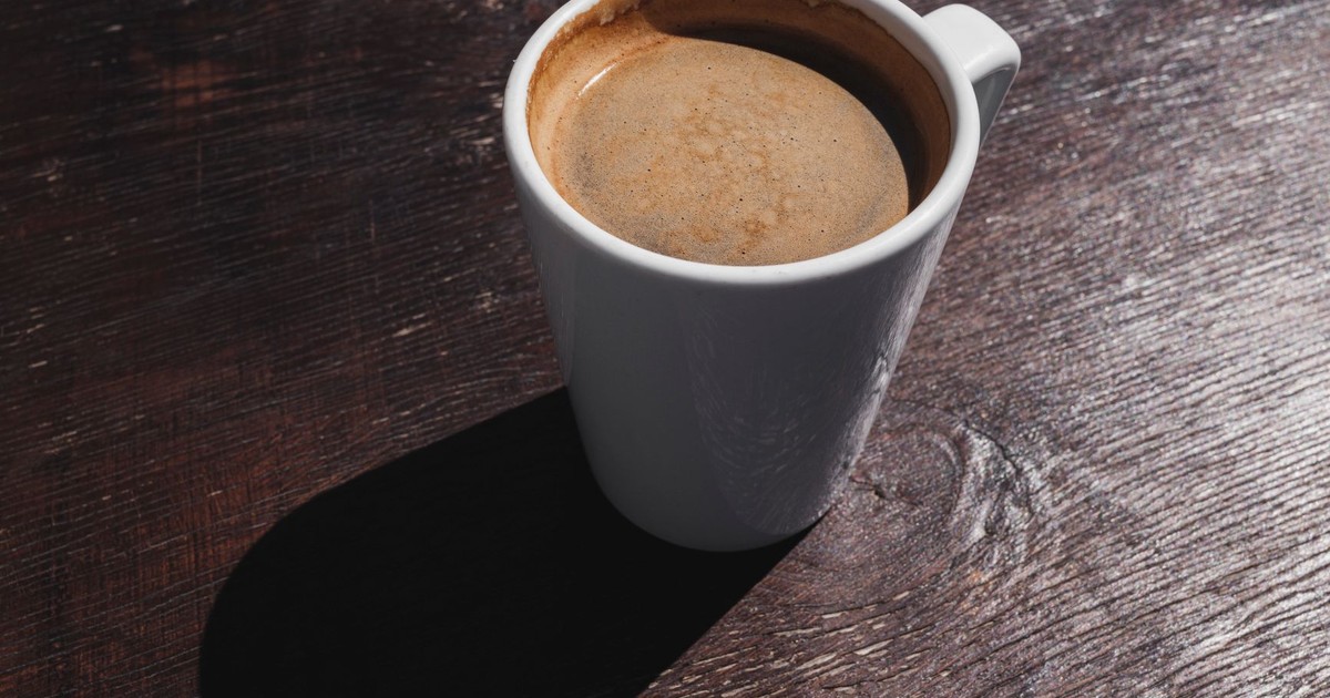 A freshly brewed cup of coffee on a rustic wooden table casting a warm morning shadow.