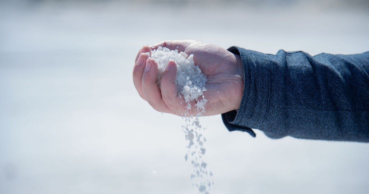 Close-up of a hand holding and pouring coarse white salt outdoors.