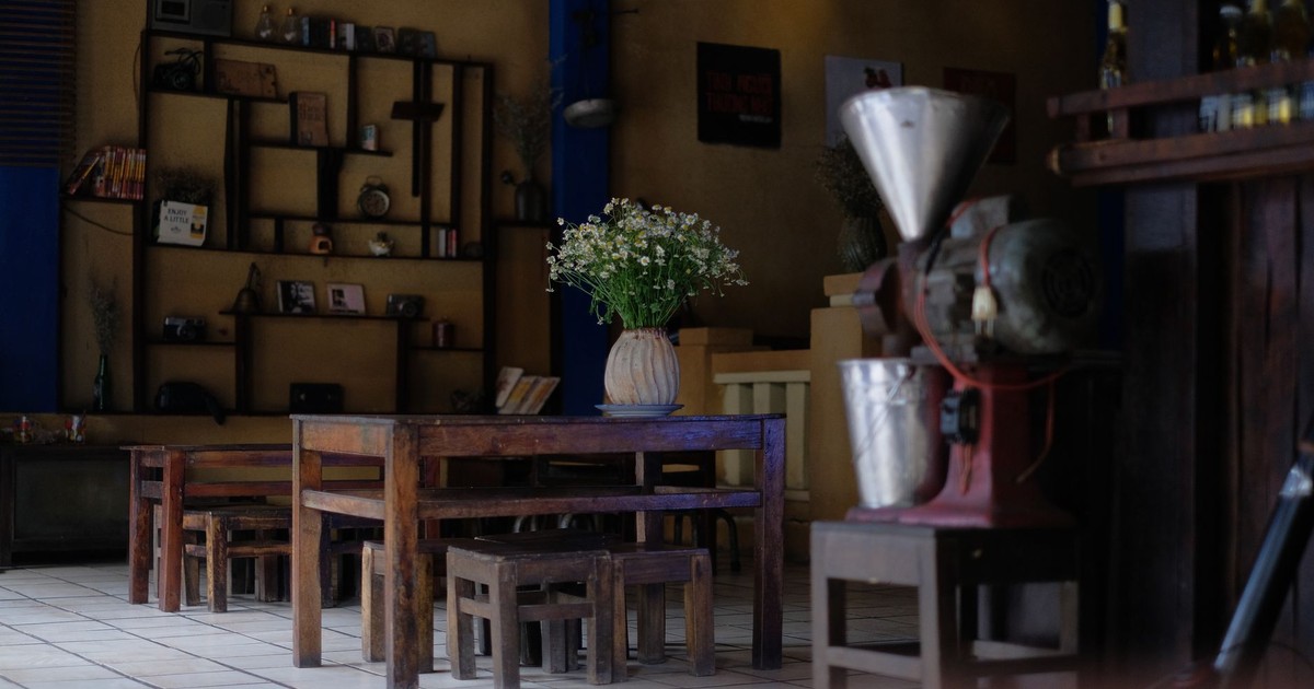 Vintage cafe interior featuring wooden furniture, a vase of white flowers, and rustic decor.
