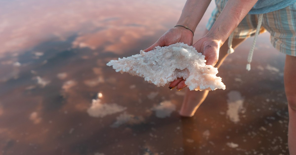 Close-up of hands holding salt crystals from a shallow saline lake at sunset.