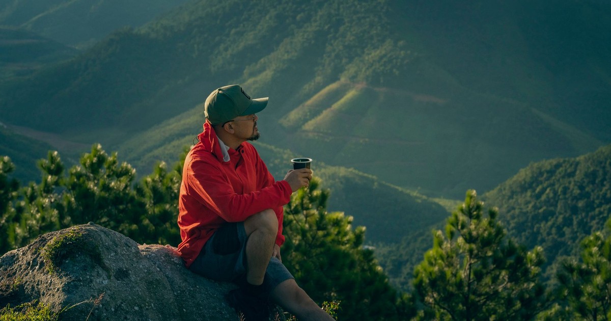 Man enjoys a serene moment in mountain scenery, sipping a drink at sunrise.