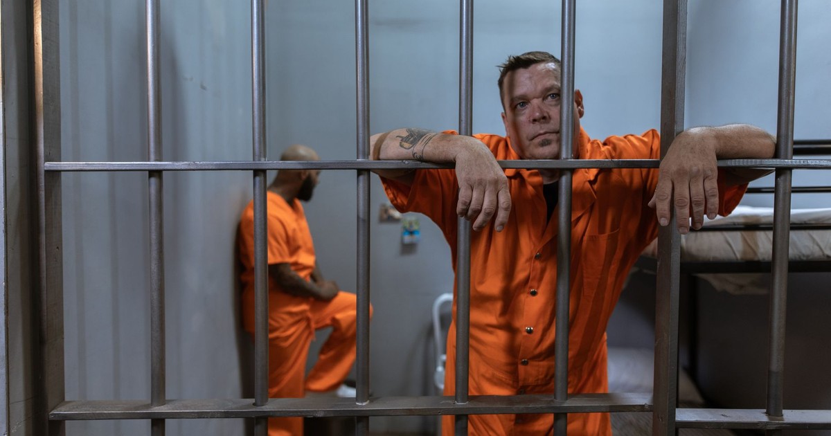 Two inmates in a prison cell wearing orange uniforms reflecting on their situation.