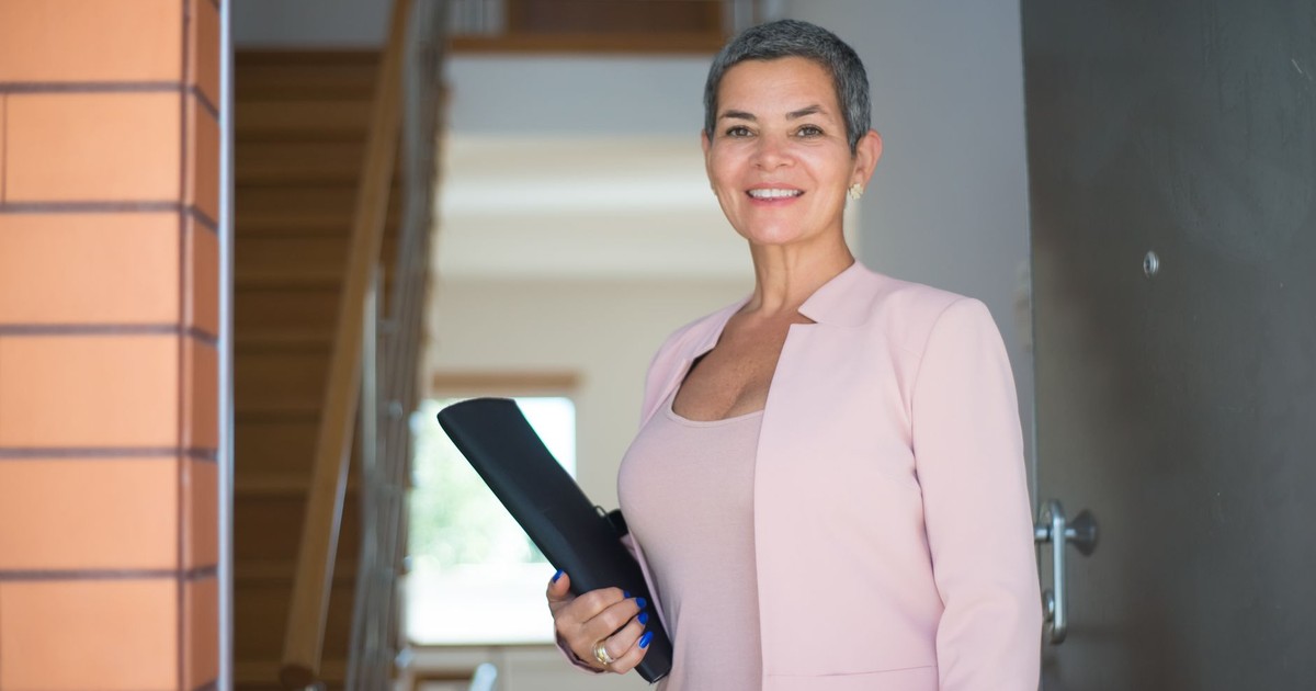 Smiling woman in pink blazer holding a document indoors, exuding confidence and professionalism.