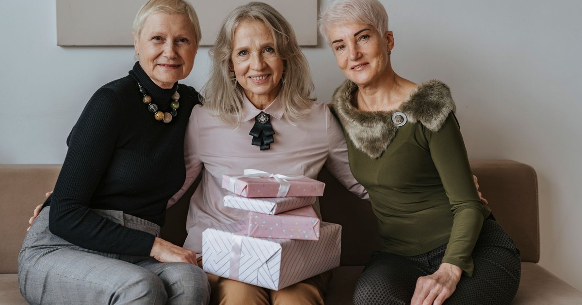 Three senior women sitting together with gifts, celebrating friendship indoors.