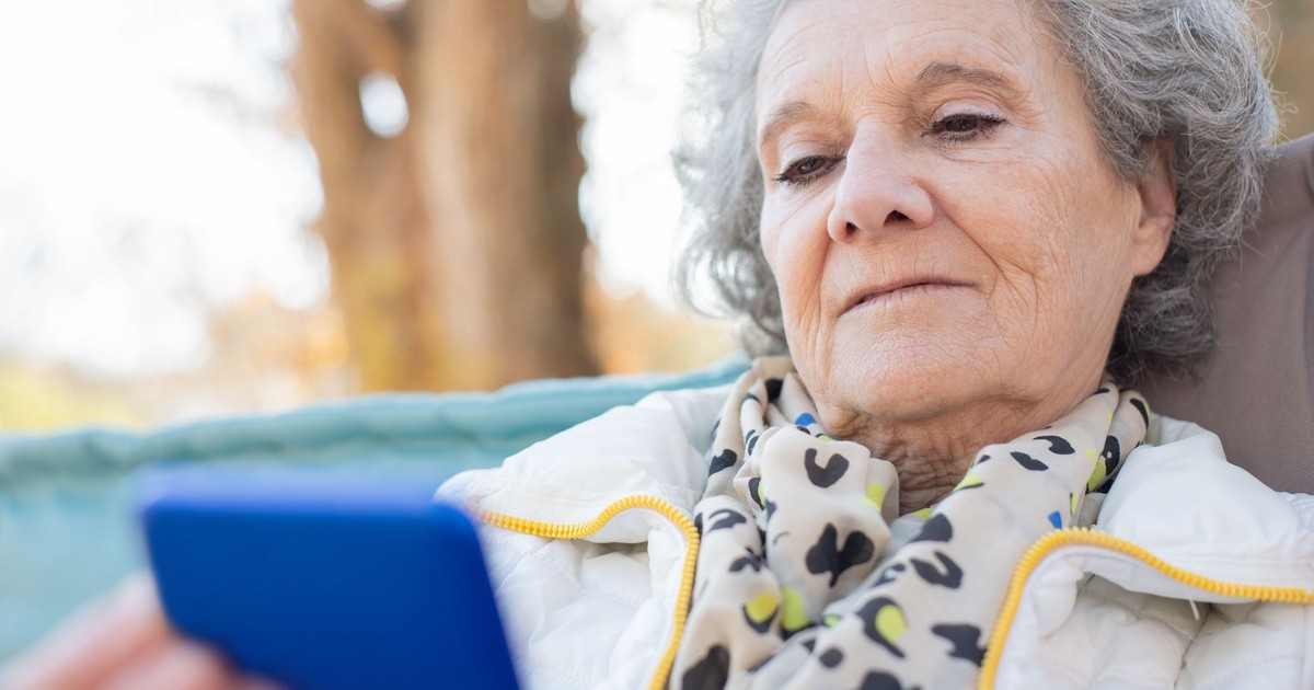 Elderly woman with a smartphone relaxing outdoors in autumn.