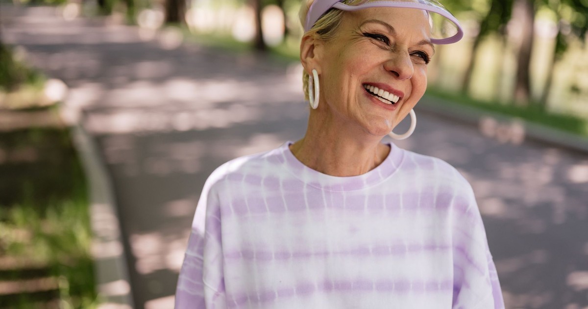 Smiling elderly woman enjoying a sunny day outdoors wearing a stylish sun visor.