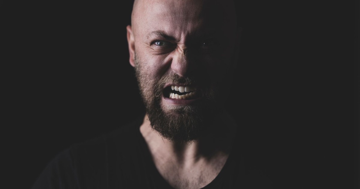 Close-up of a bald and bearded man showing a fierce expression in a dark setting.