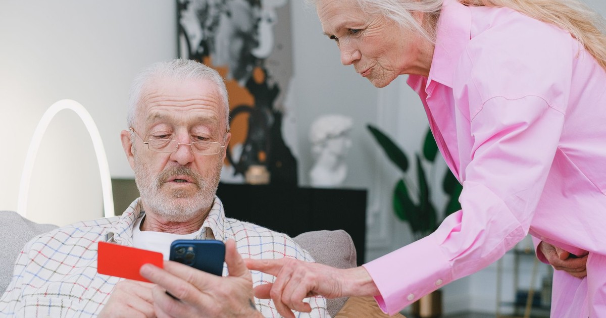Elderly couple handling credit card transaction on smartphone indoors.