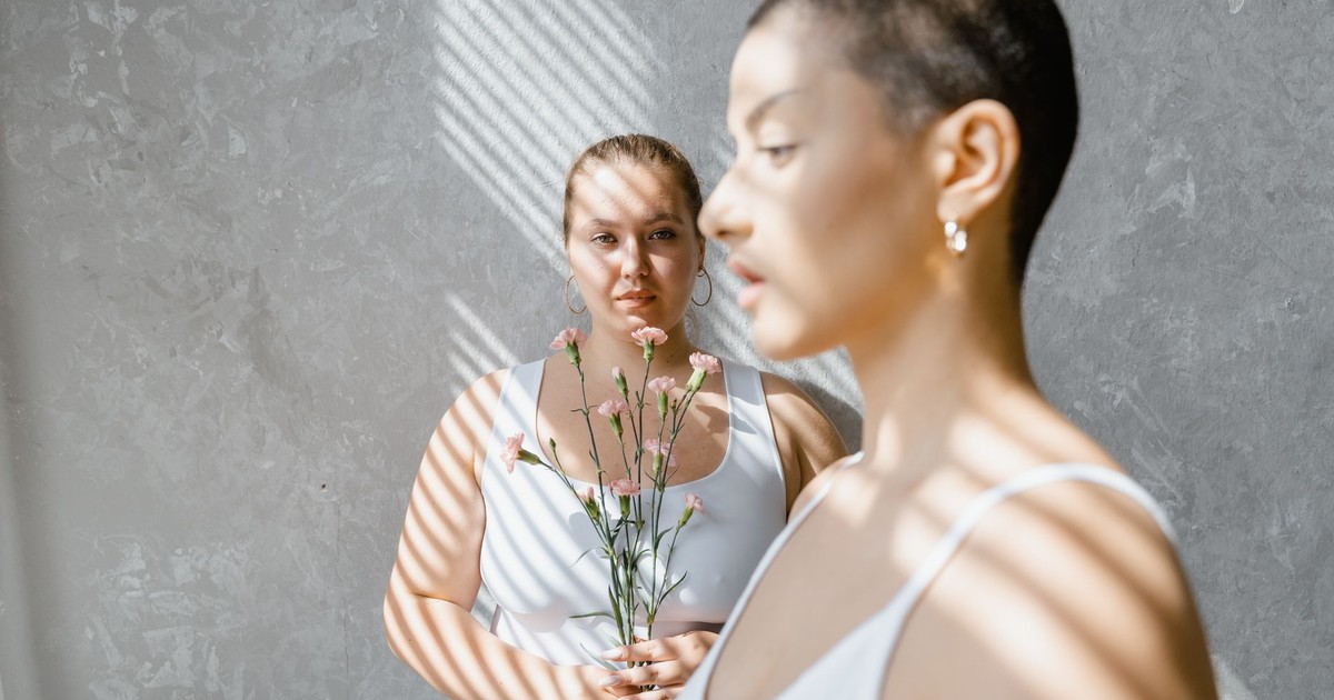 Two women in white tank tops holding flowers in an artistic indoor setting.