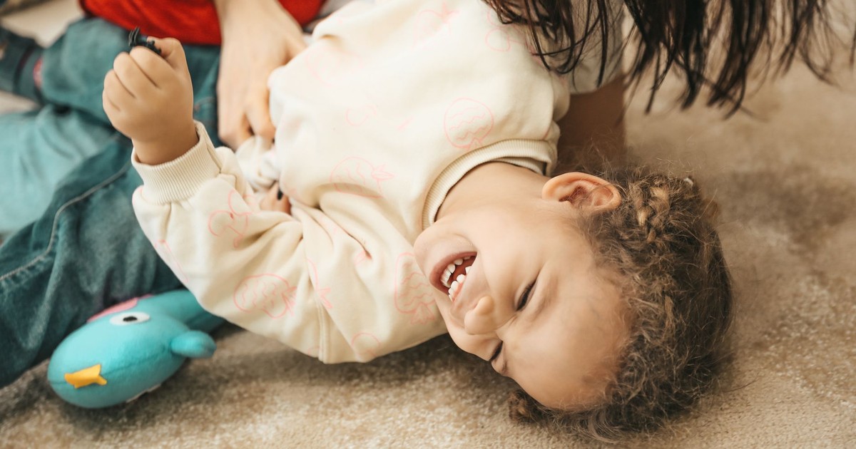 A happy child laughs while playing with a parent indoors, capturing pure joy and innocence.