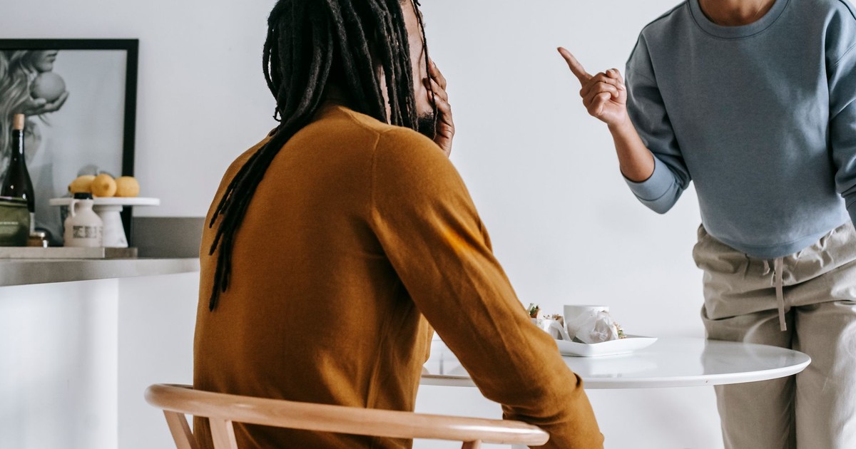 Young African American lady standing near table while having argument with guy sitting at kitchen