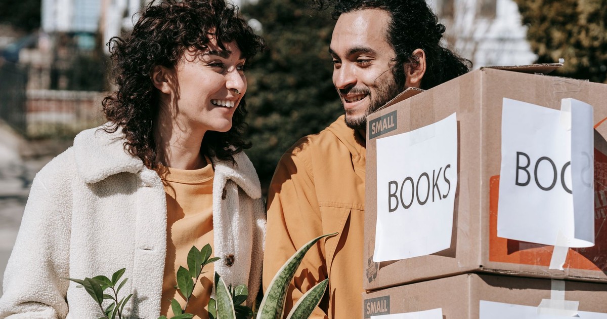 A cheerful couple moving into their new home with boxes and plants on a sunny day.