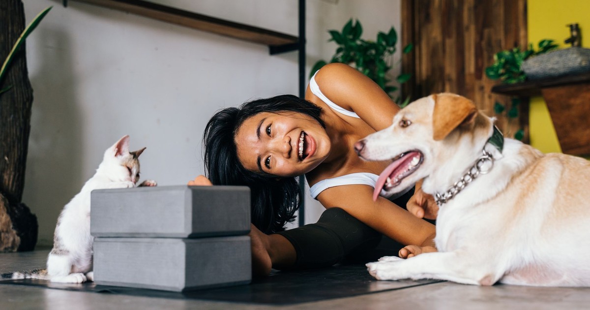 Smiling woman practicing yoga indoors with her dog and cat, embracing a healthy lifestyle.