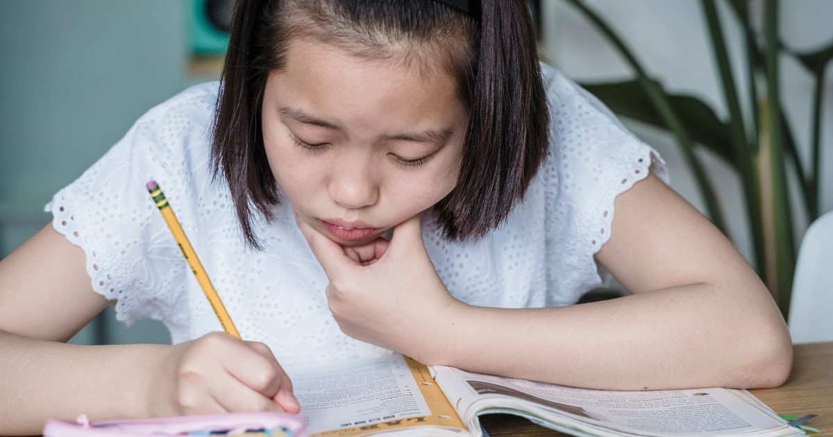 A young girl deeply engaged in homework, writing in a notebook at home.