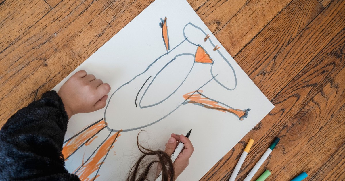 A child drawing a colorful, imaginative picture on paper with markers on the floor.