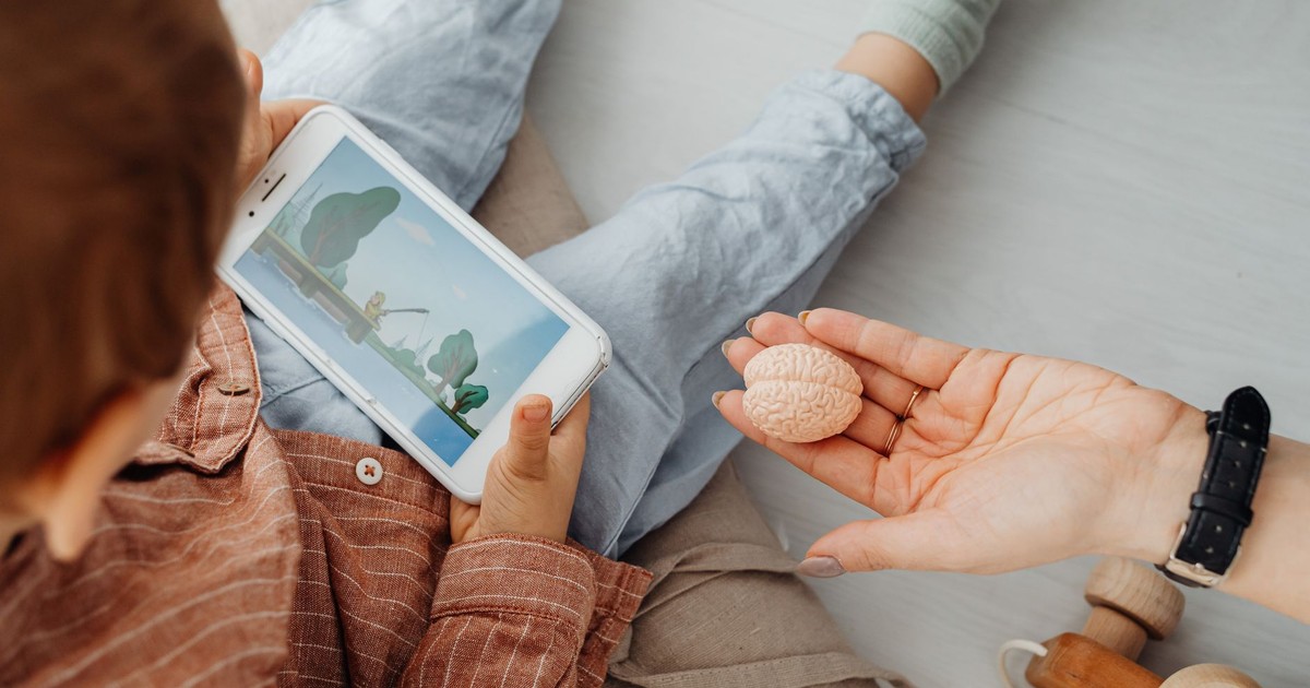 Young child engrossed in a smartphone video while holding a brain model indoors.