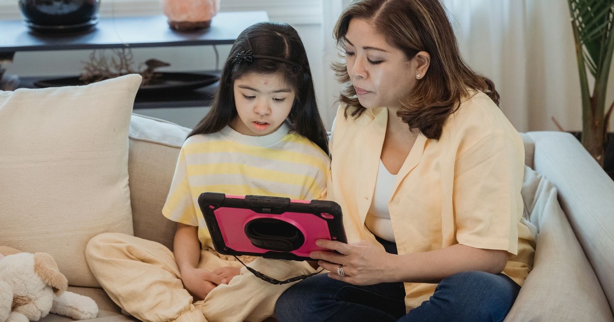 A mother and daughter bonding on the sofa using a tablet indoors.