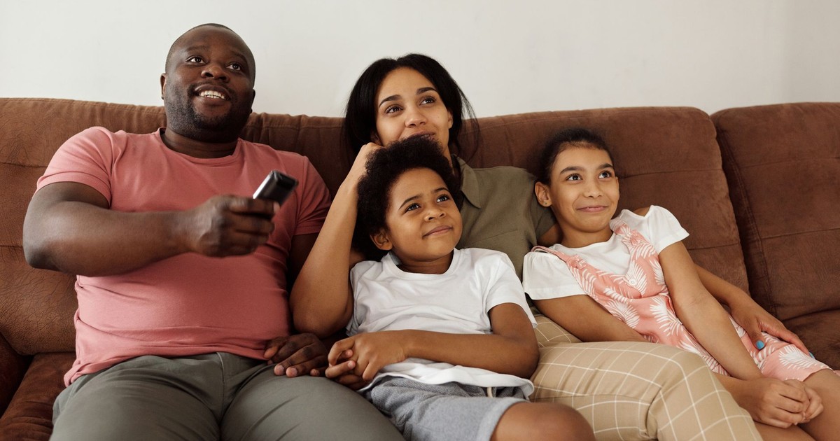 A family of four enjoying quality time together on the sofa, watching TV with smiling faces.