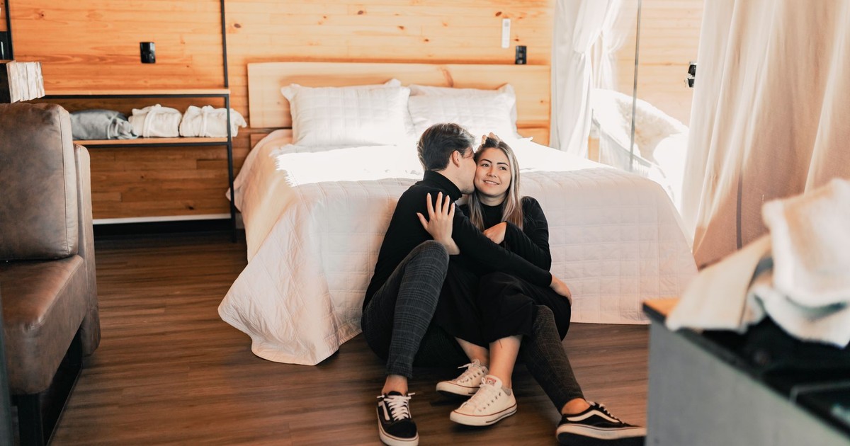 A loving couple sitting comfortably on the floor of a cozy, wooden bedroom with a relaxing atmosphere.