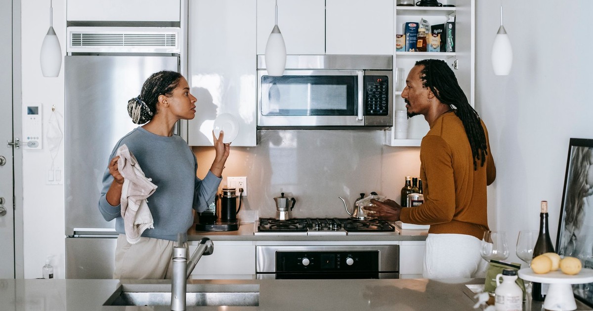 Young black woman talking to annoyed male partner while looking at each other during quarrel in house