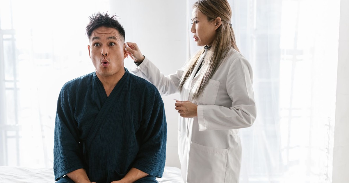 A doctor in a white coat conducts an ear exam on a patient indoors.