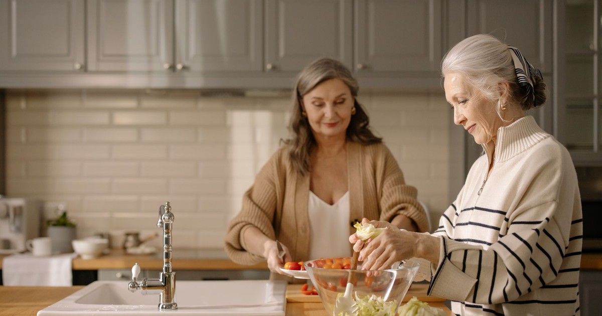 Two senior women making a fresh salad together in a cozy kitchen setting.