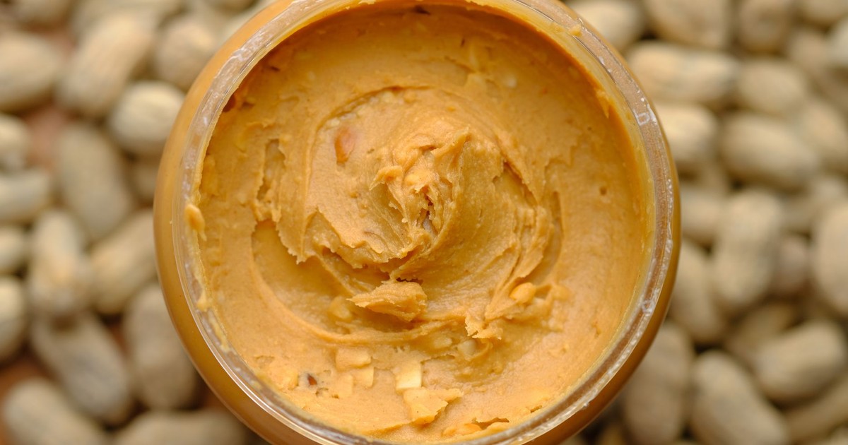 Close-up of creamy peanut butter in a glass jar surrounded by peanuts. Tasty and homemade.