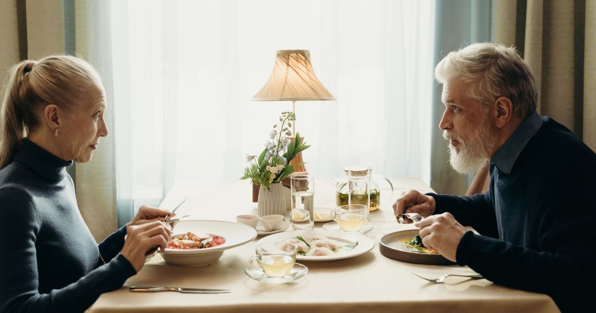 Elderly couple enjoying a meal together in a cozy, warmly lit indoor setting.