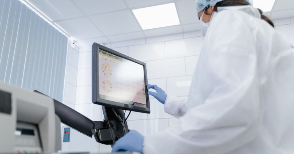 Woman in lab coat using touchscreen monitor in a modern laboratory setting.