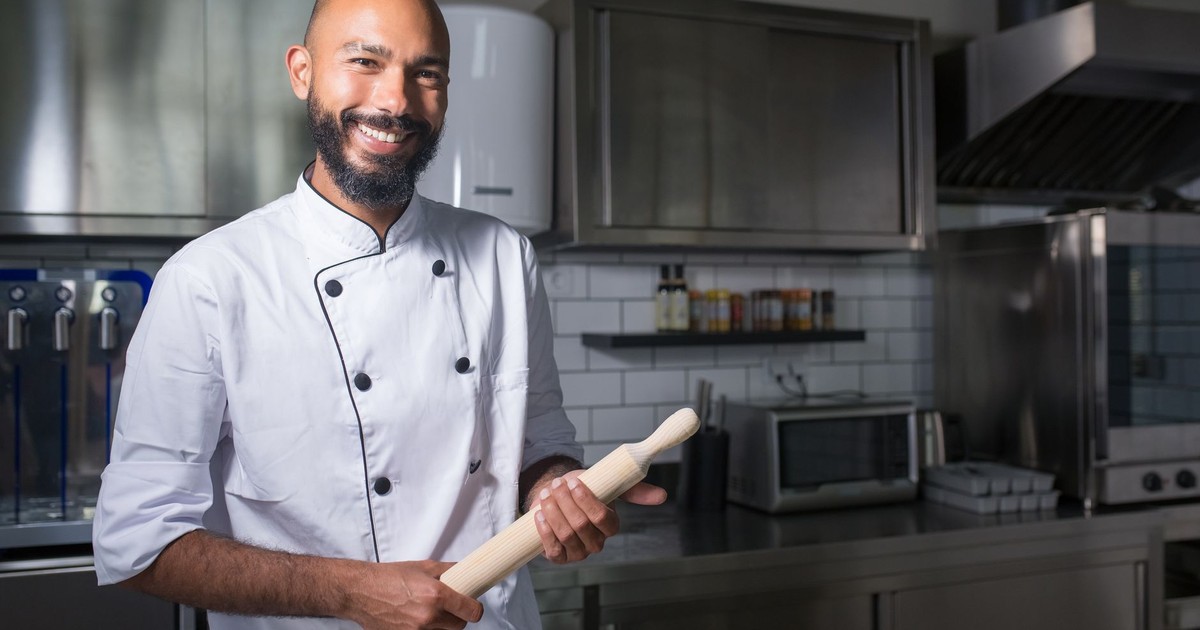 Chef in a modern kitchen holding a rolling pin, ready for cooking with a confident smile.