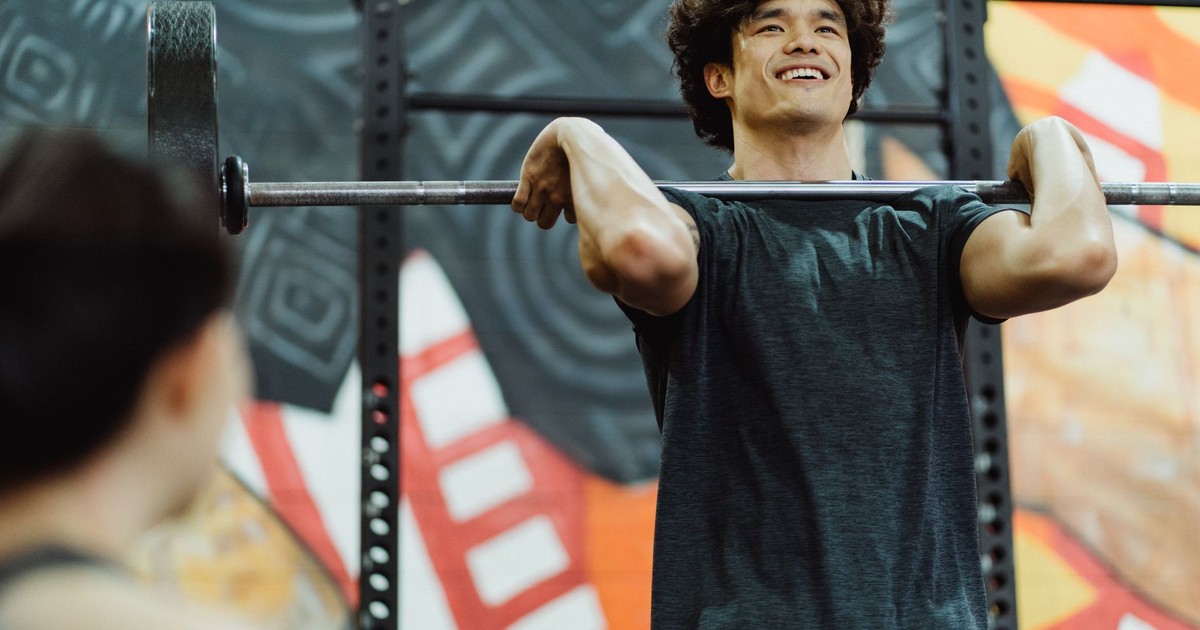 Young Asian man lifting a barbell indoors, showcasing strength and determination.