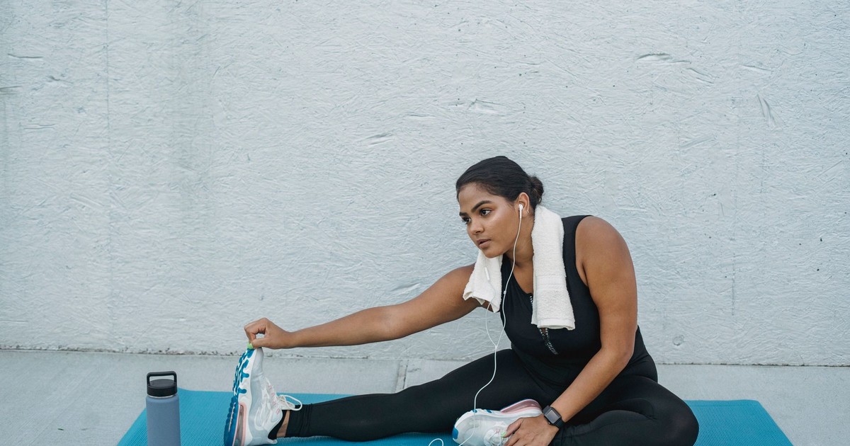 A woman in activewear stretching on a yoga mat. Listening to music during her fitness routine.