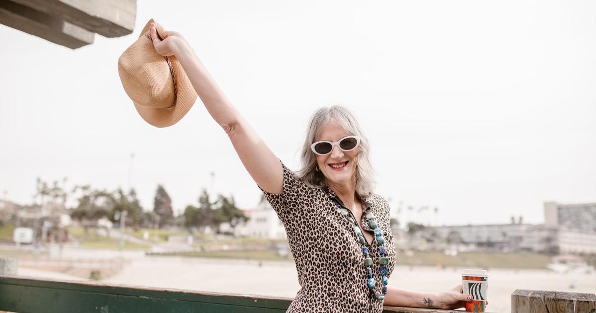 Stylish senior woman with hat at the beach, embracing life joyfully.
