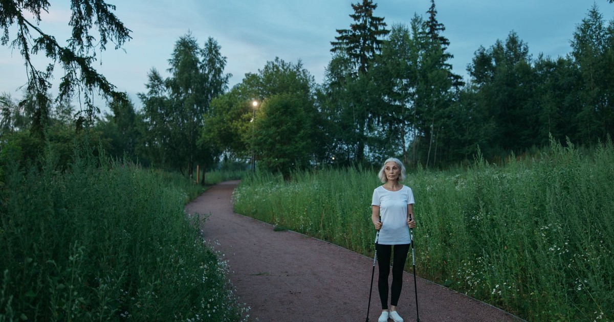 Senior woman exercising with Nordic walking poles in a peaceful green park during daytime.
