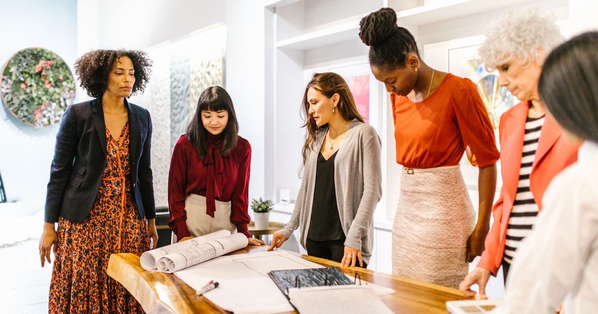 A diverse group of professional women discussing plans in a modern office setting.