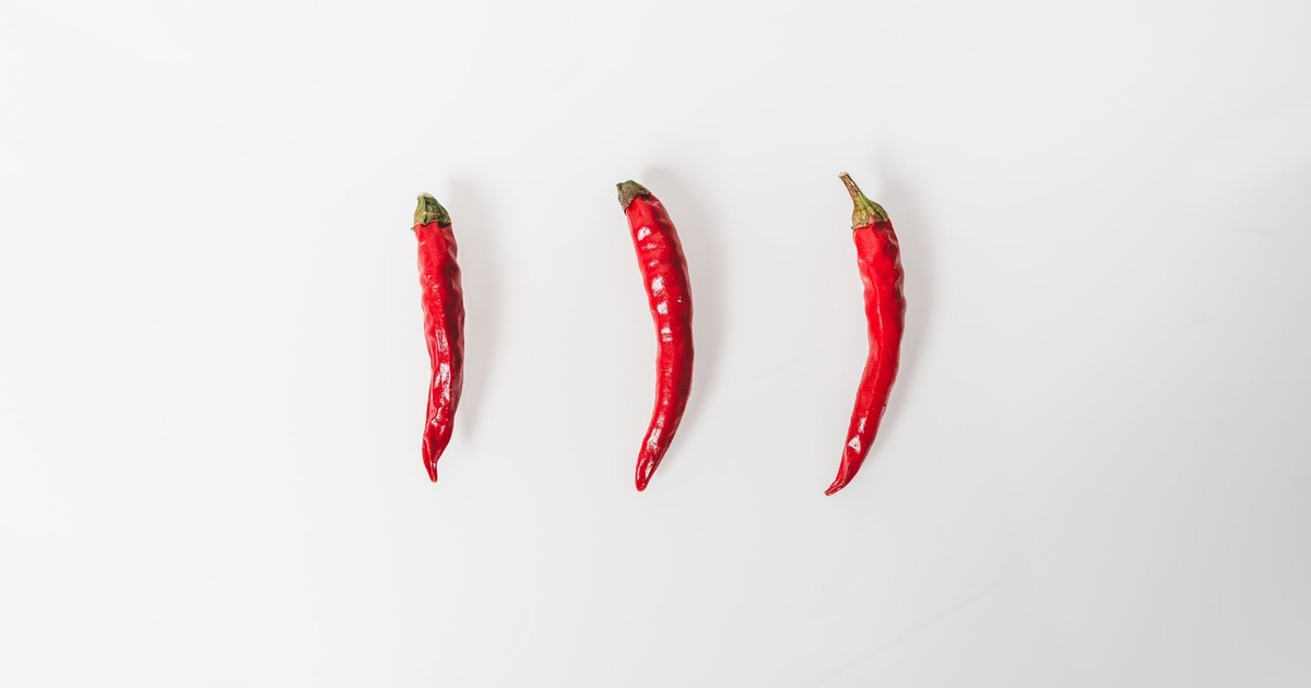 Three red chilies arranged on a white background in a minimalist style.