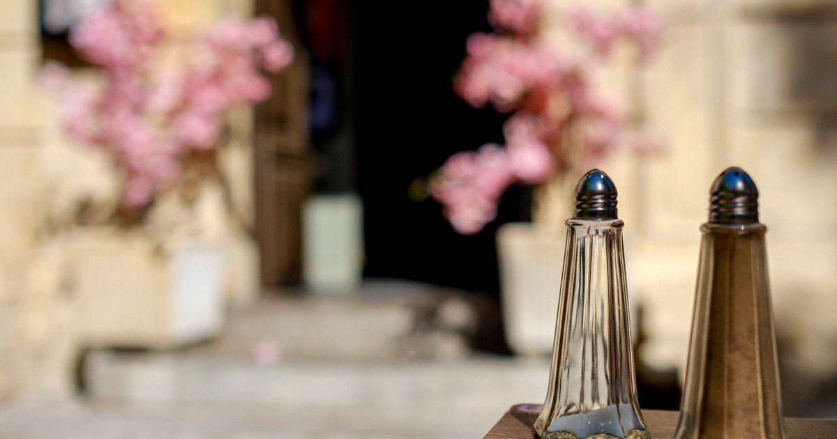 Close-up of salt and pepper shakers on table with blurred floral background in Arles, France.