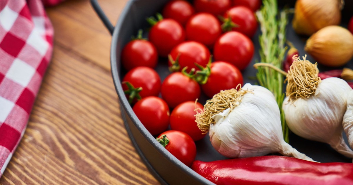 A vivid display of fresh Mediterranean vegetables on a wooden table with a pan.