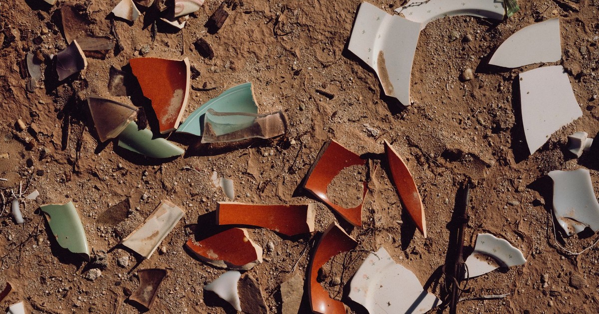 A collection of broken ceramic pieces scattered on a dirt ground under sunlight.