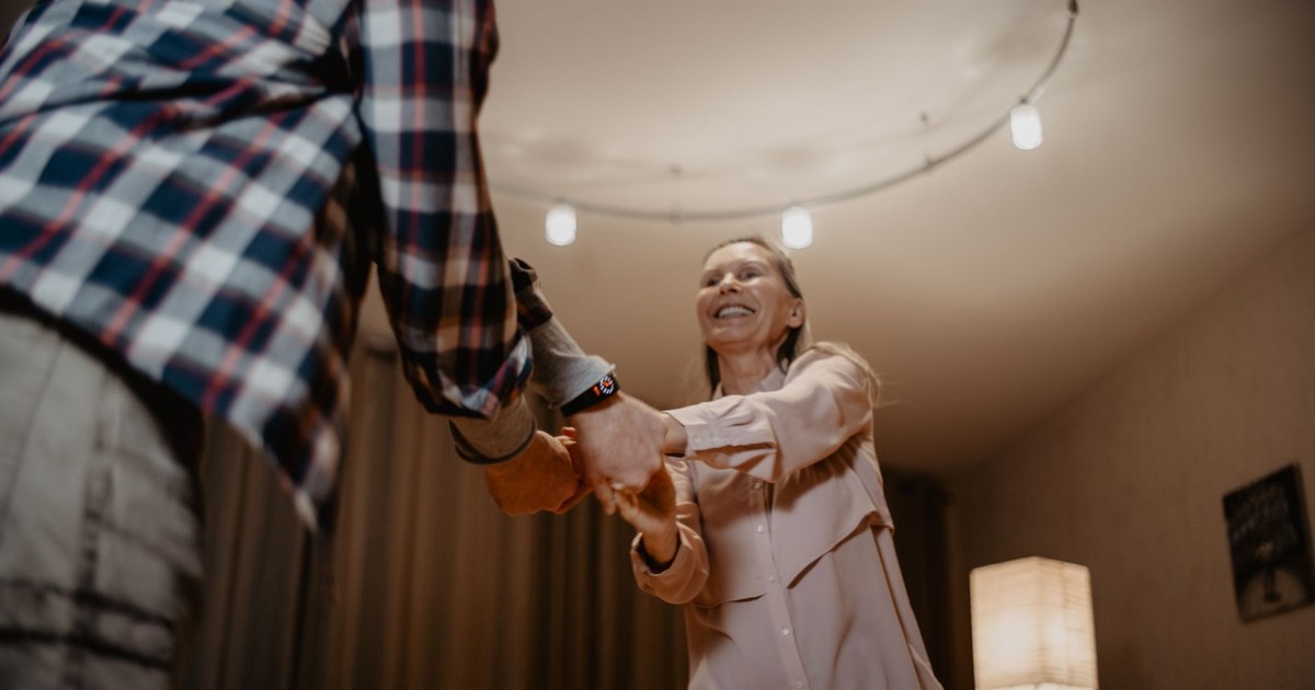A happy senior couple dancing joyfully indoors, embracing a moment of togetherness.