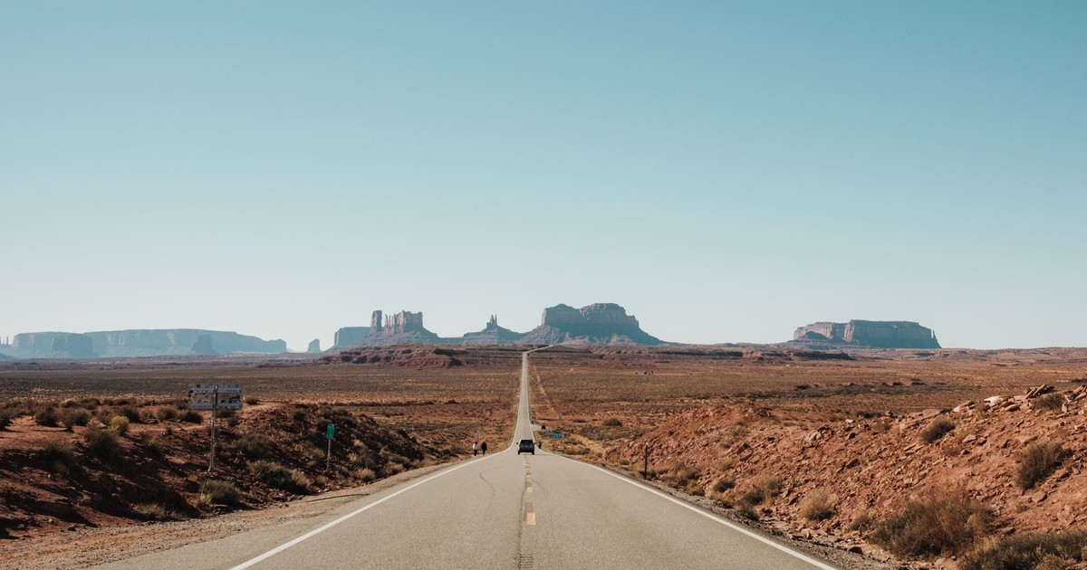 Scenic road stretching into Monument Valley under a clear sky.