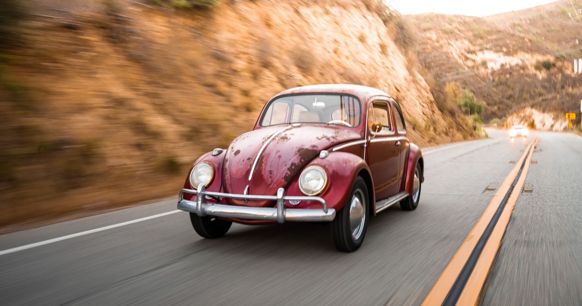 Classic red Volkswagen Beetle driving on a winding scenic highway with blurred background.