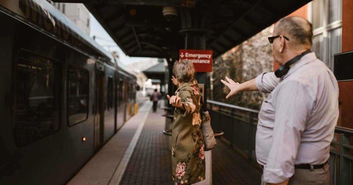 A couple waving goodbye at a train station platform as the train departs.