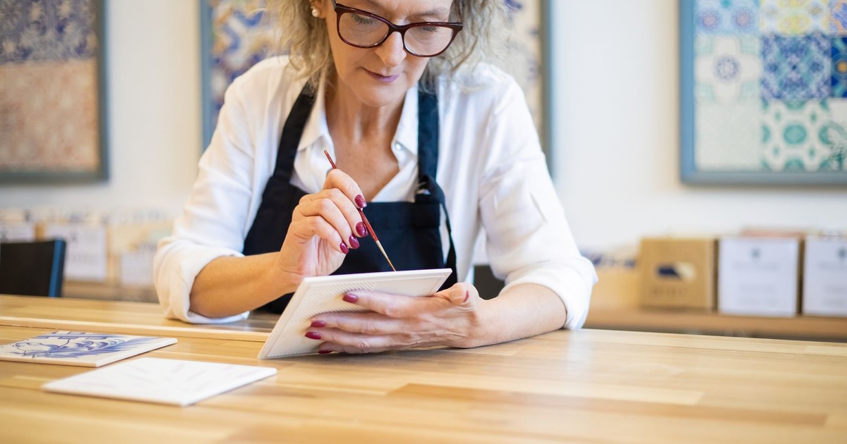 Senior woman painting a tile in Portugal, showcasing artistic passion and creativity in a focused setting.